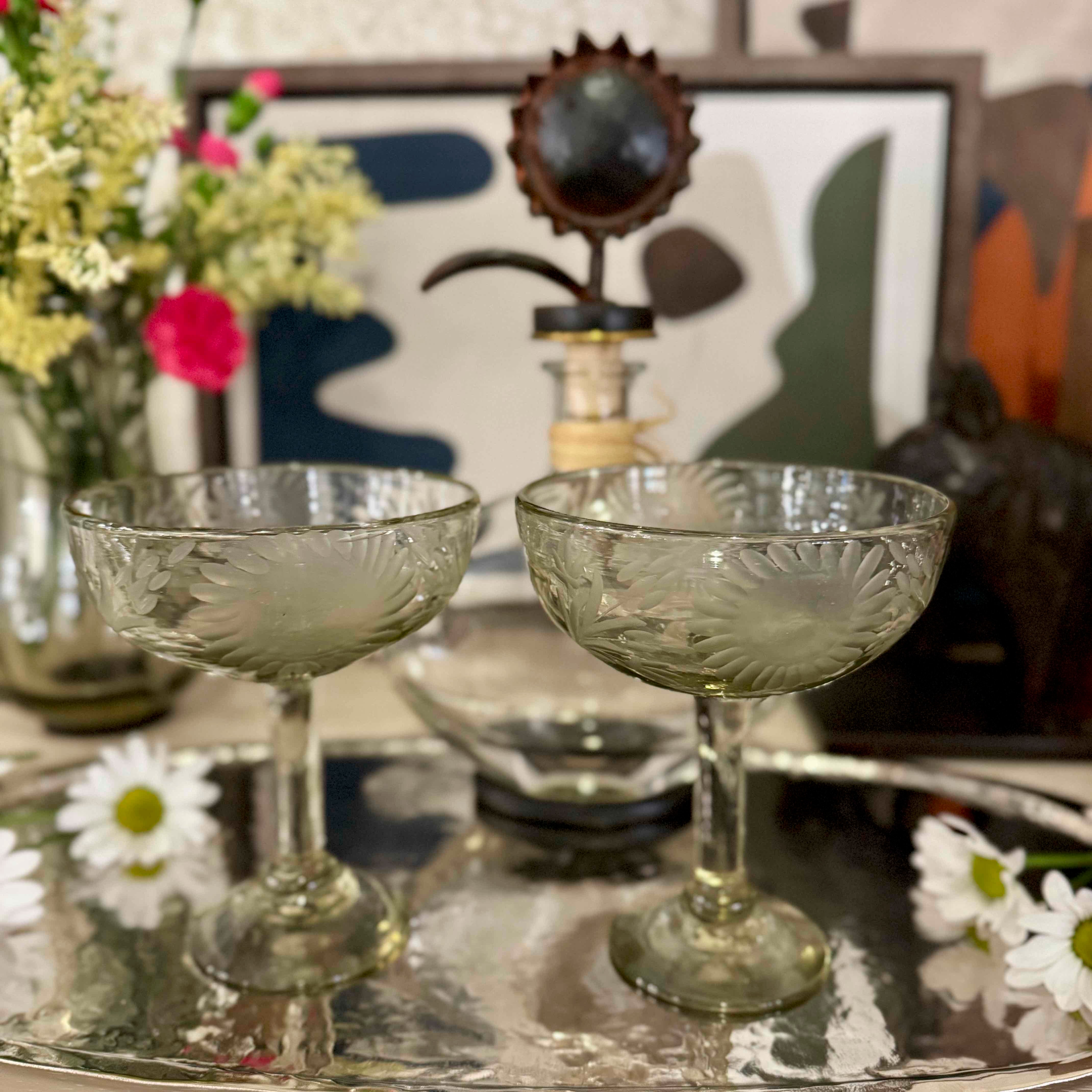 Two vintage-style glass coupes on a reflective surface with a blurred decorative background.