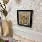 Framed embroidered artwork on a wall with decorative wallpaper and decor items.