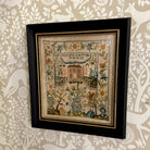 Framed embroidered sampler with decorative elements on a patterned wall.