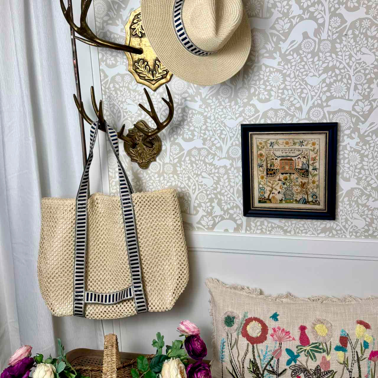 Woven bag with striped strap hanging on a coat rack against a decorative wall.