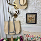 Woven bag with striped strap hanging on a coat rack against a decorative wall.