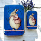 Two tin boxes with a rabbit illustration on a wooden surface with lavender flowers.