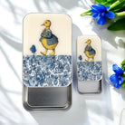 Two tin containers with a duck illustration and floral pattern on a white surface with blue flowers.