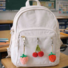 White backpack with fruit-themed keychains on a classroom desk