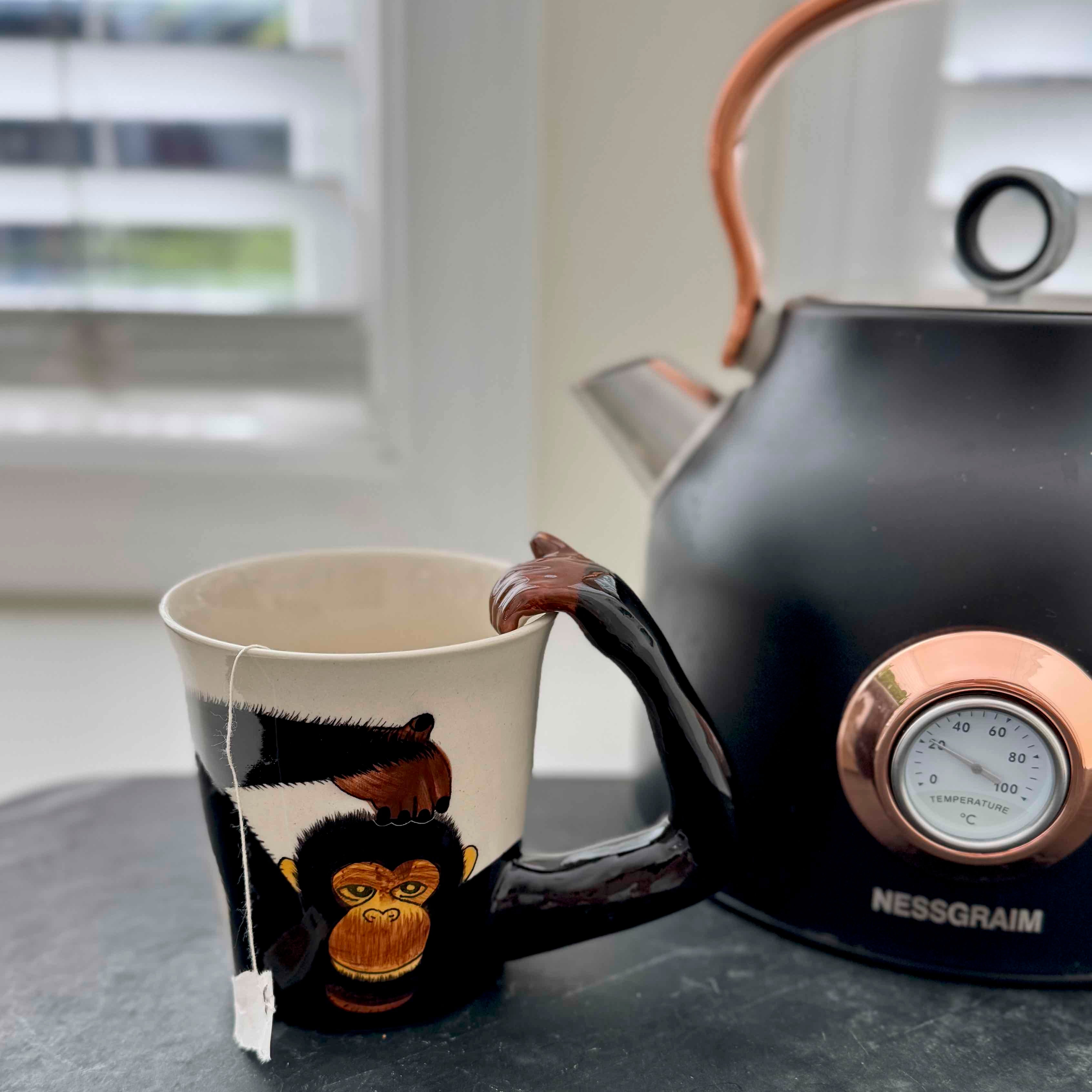 Black teapot with a monkey design on the spout and a white mug with a tea bag inside, on a surface.