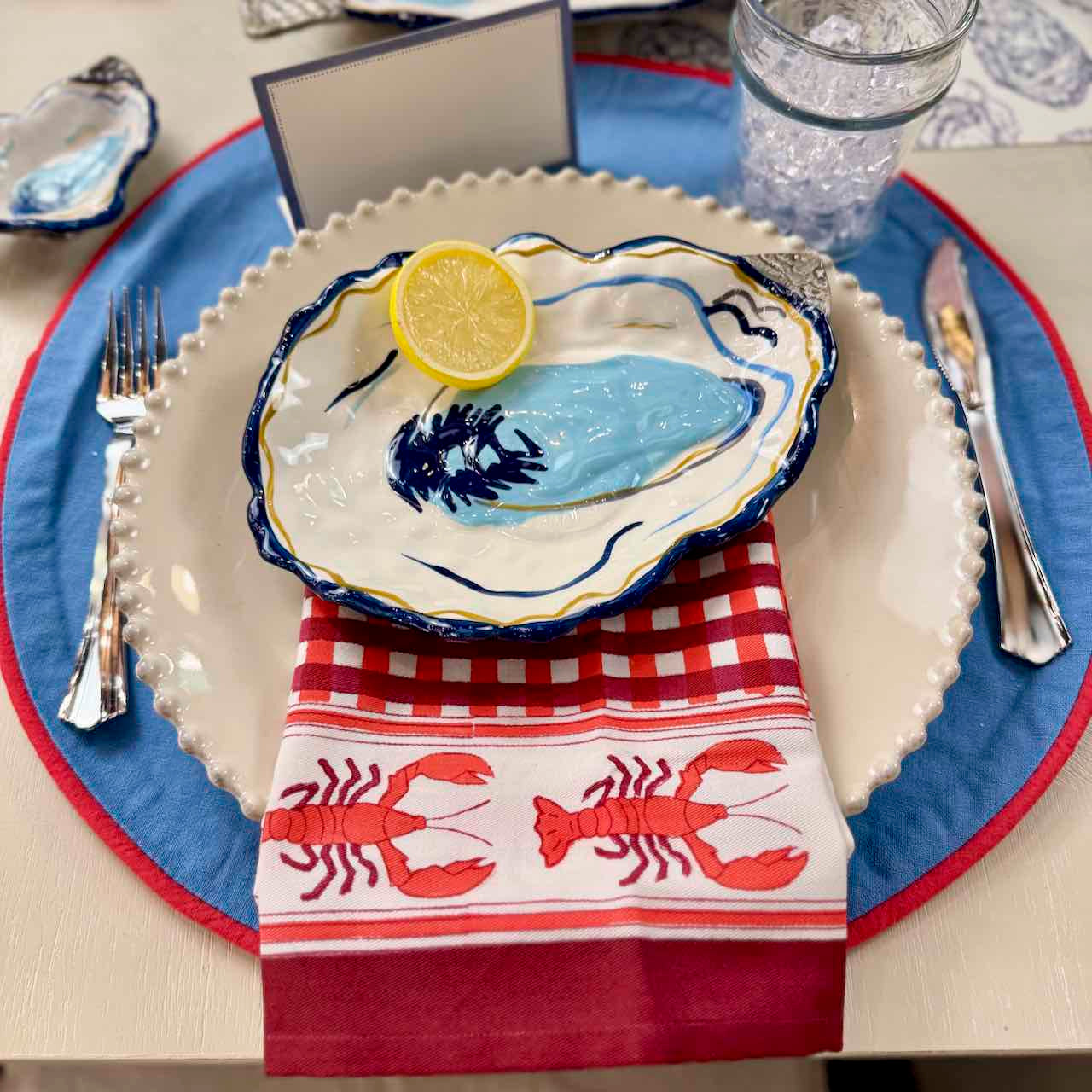 Nautical-themed table setting with oyster shell plate, lemon, and lobster patterned napkin.