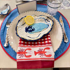 Nautical-themed table setting with oyster shell plate, lemon, and lobster patterned napkin.