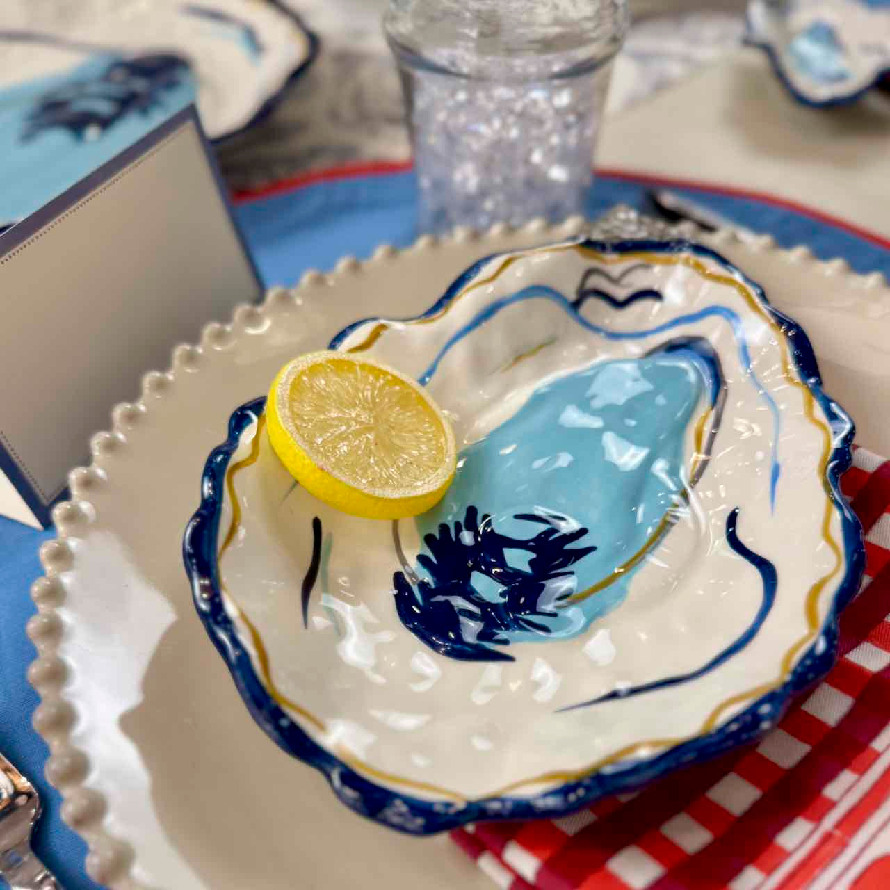 Decorative ceramic oyster shell with a lemon slice on a checkered tablecloth.