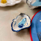 Ceramic oyster-shaped dish on a light wooden surface with a fork and other items in the background.