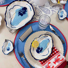 Table setting with oyster-themed plates and napkins on a blue and white tablecloth.