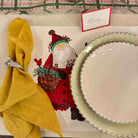 Christmas-themed table setting with Santa Claus card, yellow napkin, and green plate.