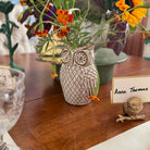 Owl-shaped vase with flowers on a wooden table with a name card.