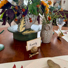 Decorative table setting with flowers, butterfly, owl vase, and name card on a wooden table.