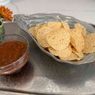 Tortilla chips on a plate with a bowl of salsa on a gray surface.