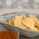 Tortilla chips in a gray bowl with a side of salsa on a textured surface.