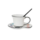 White mug with black rim on a matching saucer with color swatches, accompanied by a black spoon.