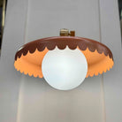 Decorative ceiling light fixture with brown and orange scalloped design on a plain background