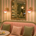 Pink sofa with decorative pillows in a room with striped wallpaper and a mirror.