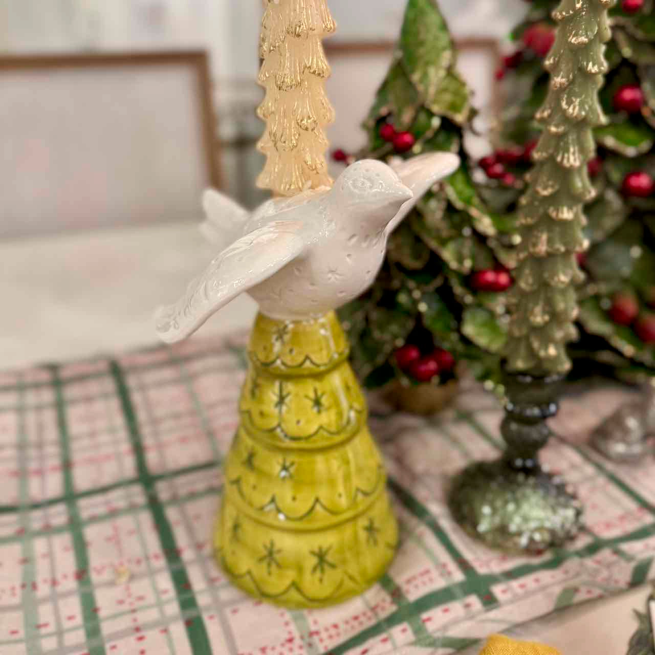 Decorative bird figurine on a yellow stand with Christmas trees in the background