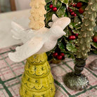 Decorative yellow candle holder with white doves against a Christmas tree background