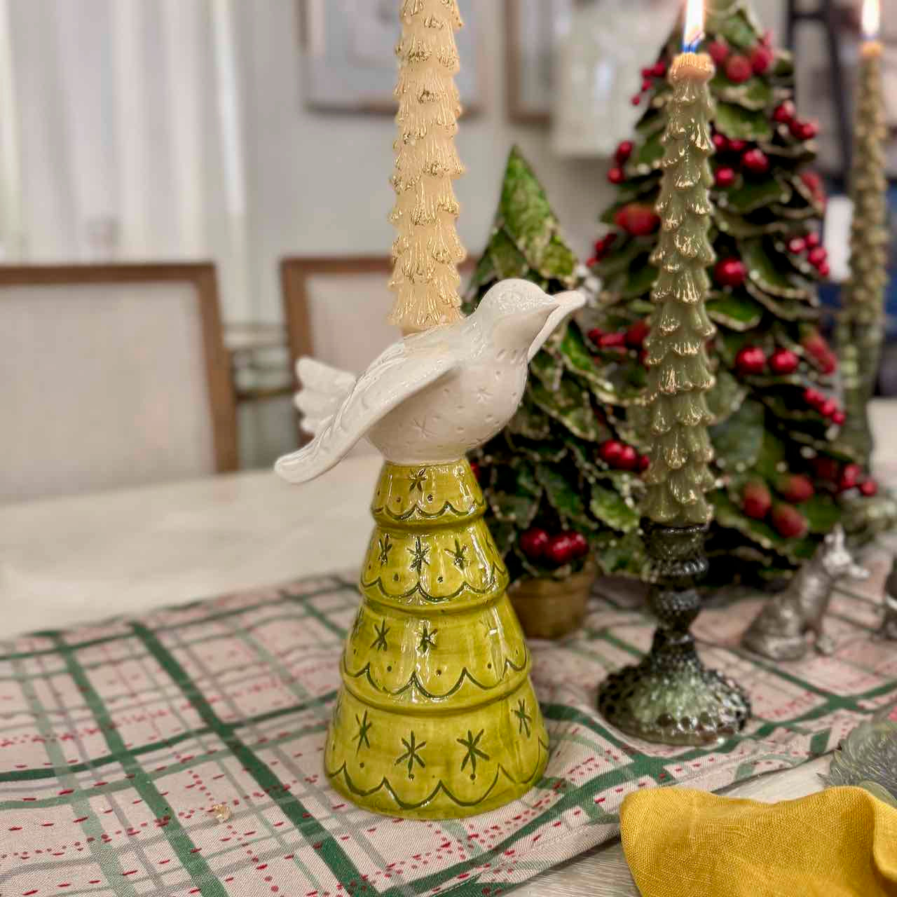Decorative candle holder with a bird design on a table with Christmas trees in the background.