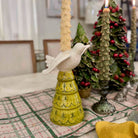 Decorative candle holder with a bird design on a table with Christmas trees in the background.