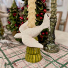 Decorative bird figurine on a green base with a Christmas tree in the background