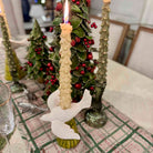 Decorative candle holder with a lit candle on a table with a Christmas tree in the background.