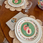 Decorative plate with peach design on a wooden table with placemats and napkins.