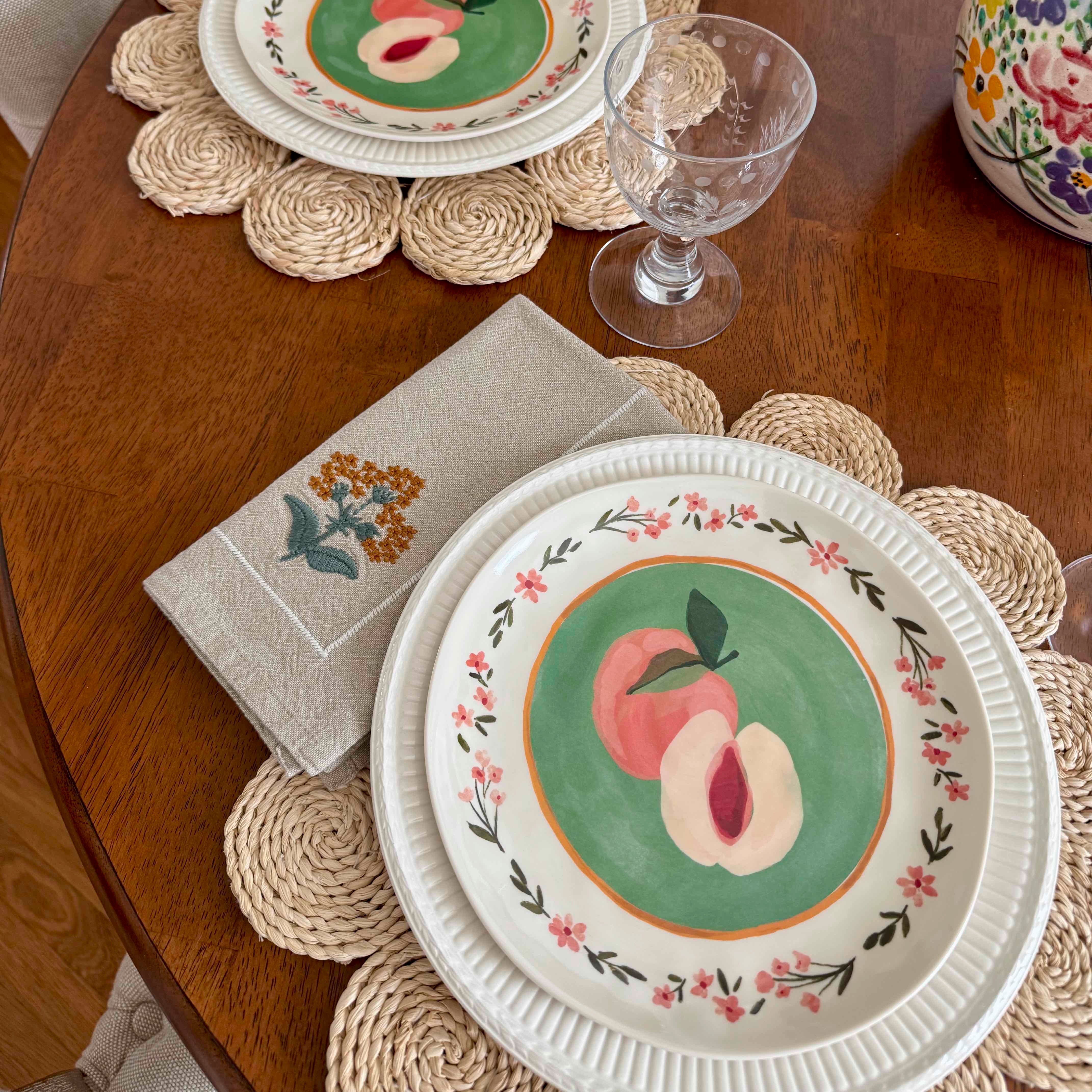 Decorative plate with peach design on a wooden table with placemats and napkins.
