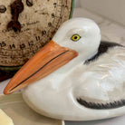 Ceramic pelican figure with an antique scale in the background