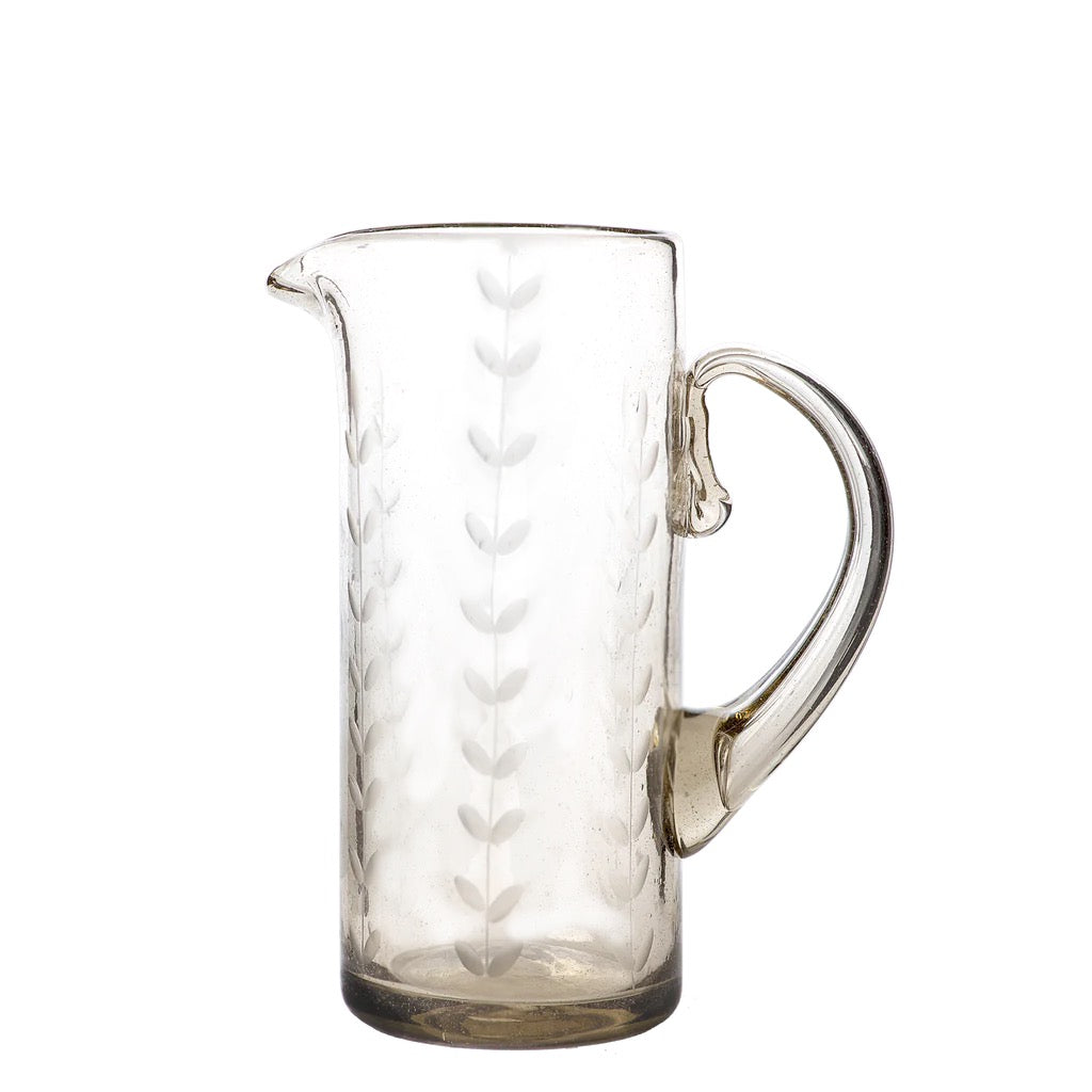 A clear, mouth-blown glass pitcher with vertical etched laurel leaves and a rustic shape, suitable for serveware or as a decorative vase.