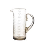 A clear, mouth-blown glass pitcher with vertical etched laurel leaves and a rustic shape, suitable for serveware or as a decorative vase.