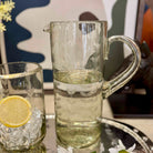 Clear glass pitcher and glass with lemon slice and ice on a table.