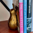 Gold pear-shaped object leaning against a stack of books on a wooden surface.