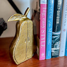Gold pear-shaped object next to a row of books on a wooden surface