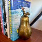 Gold pear-shaped object in front of a book titled 'Women on Waves' on a wooden surface.