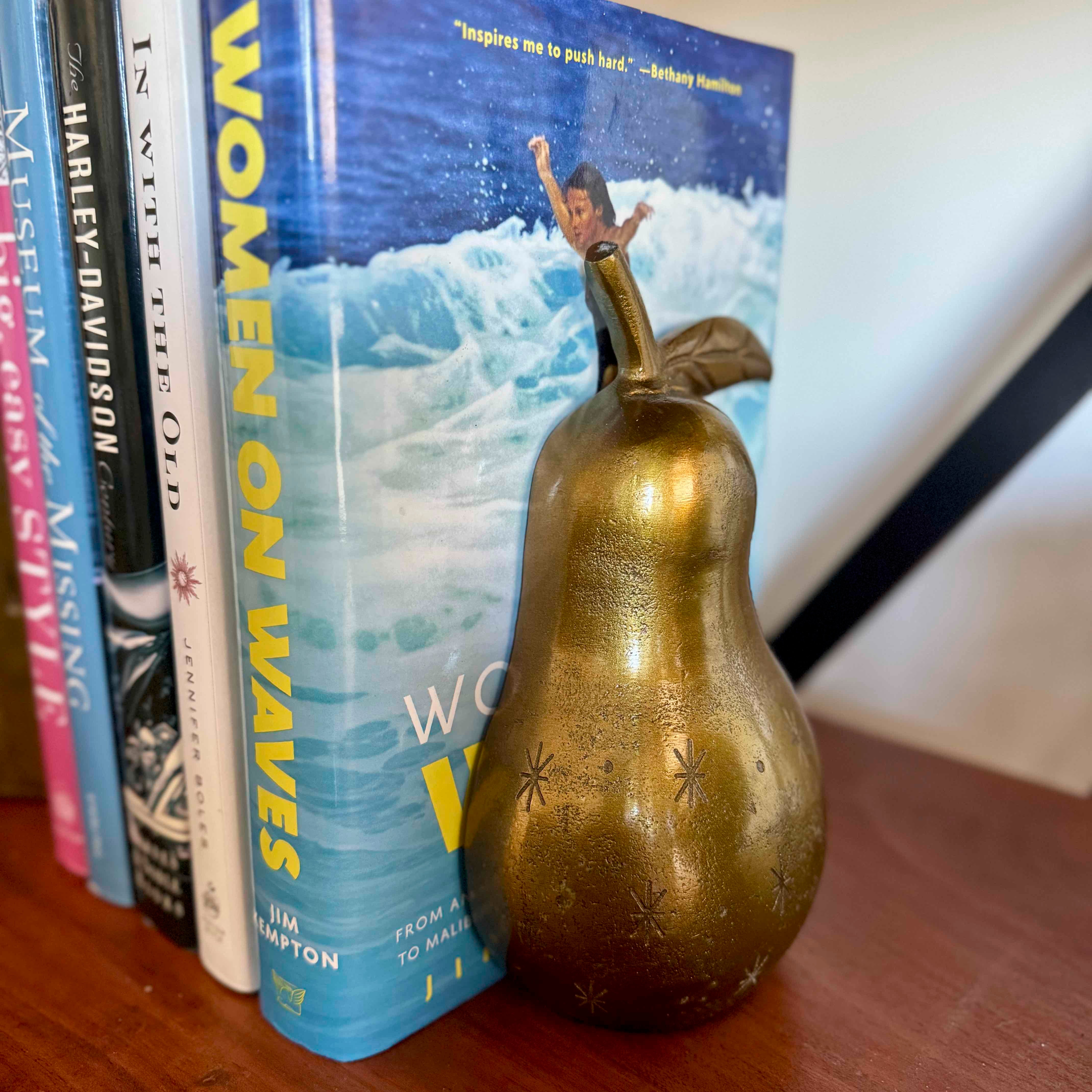 Gold pear-shaped object in front of a book titled 'Women on Waves' on a wooden surface.