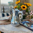 Silver pitcher with a fox handle on a table with sunflowers in the background