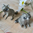 Two silver animal figurines on a wooden surface with flowers in the background.