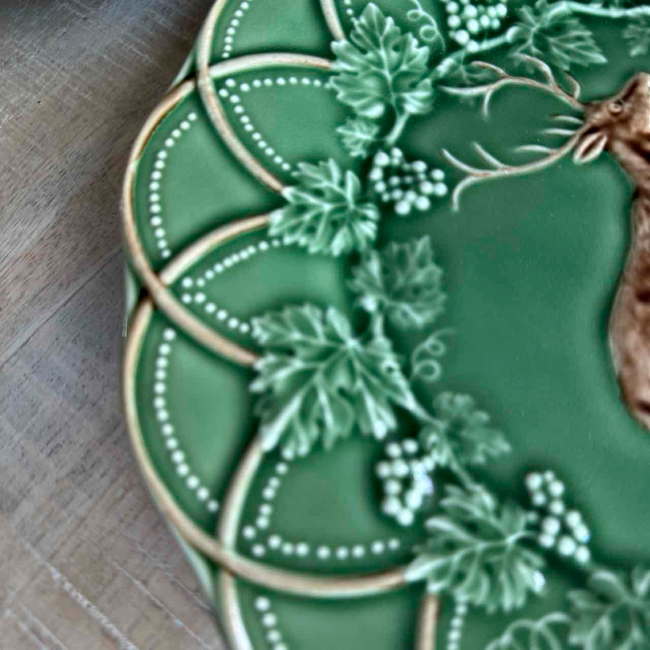 Decorative green ceramic plate with floral patterns on a wooden surface