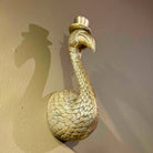 Gold flamingo door knocker with a top hat on a beige wall.