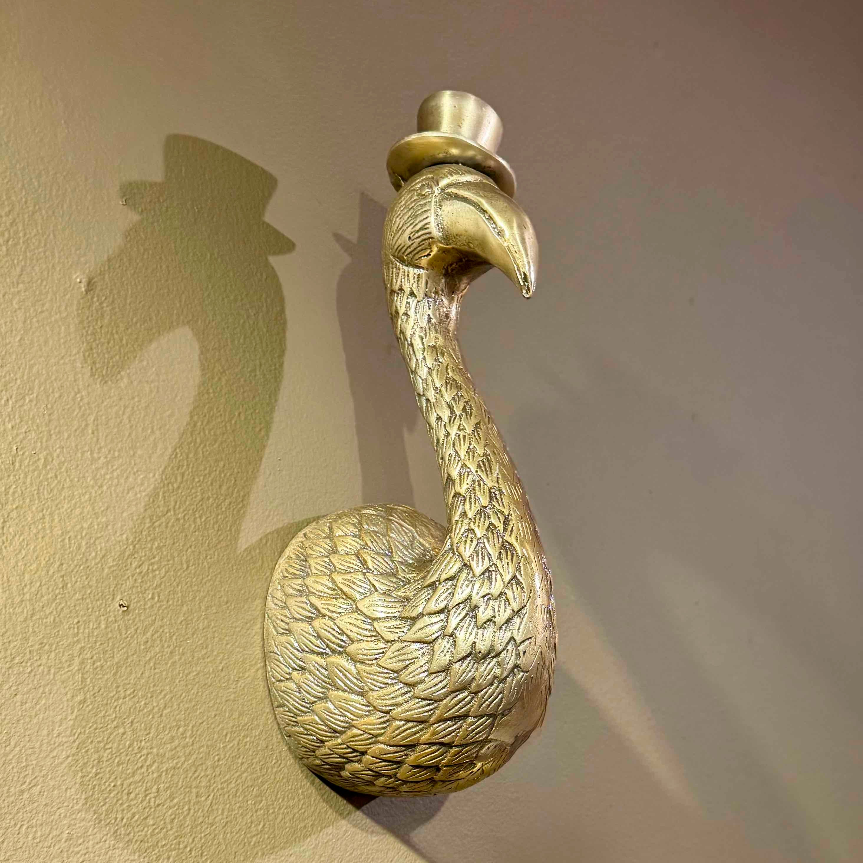 Gold flamingo door knocker with a top hat on a beige wall.