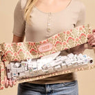 A person holding a floral zippered case filled with white mahjong tiles. The case has a pink and green botanical pattern, a clear front window, and a small pink label reading 'Mahjong Tiles'.