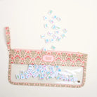 A clear zip pouch with a pink and green floral patterned fabric trim, featuring a small pink brand label that reads 'THE TIES'. The pouch is shown open with several small illustrated tiles scattered above and inside it, on a plain off-white background.