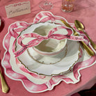 Table setting with a pink ribbon-themed placemat and cutlery on a pink tablecloth.
