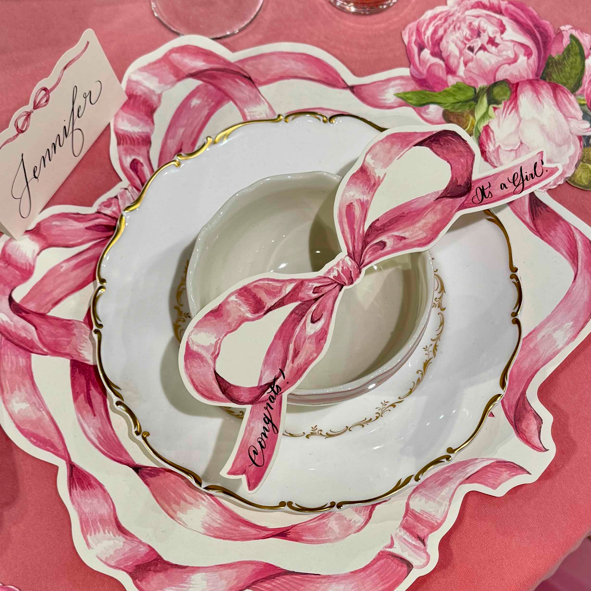 Decorative place setting with pink ribbons and 'It's a Girl' card on a pink background