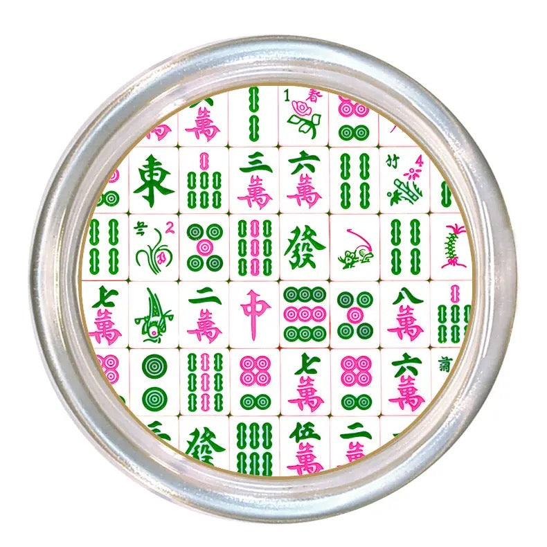 A round silver-framed clock or wall decor piece featuring a Mahjong-style tile pattern in green, pink, and white on the face, shown against a plain white background.