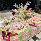 Decorative table setting with floral tablecloth, plates, and flowers outdoors.