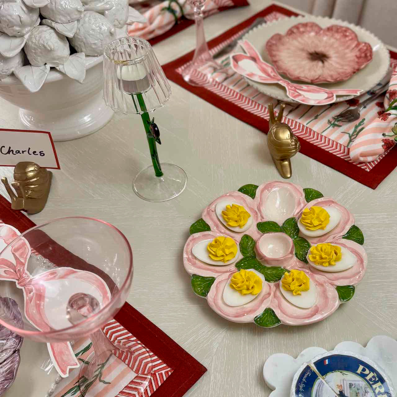 Decorative table setting with a plate of deviled eggs and flowers, wine glasses, and place cards.